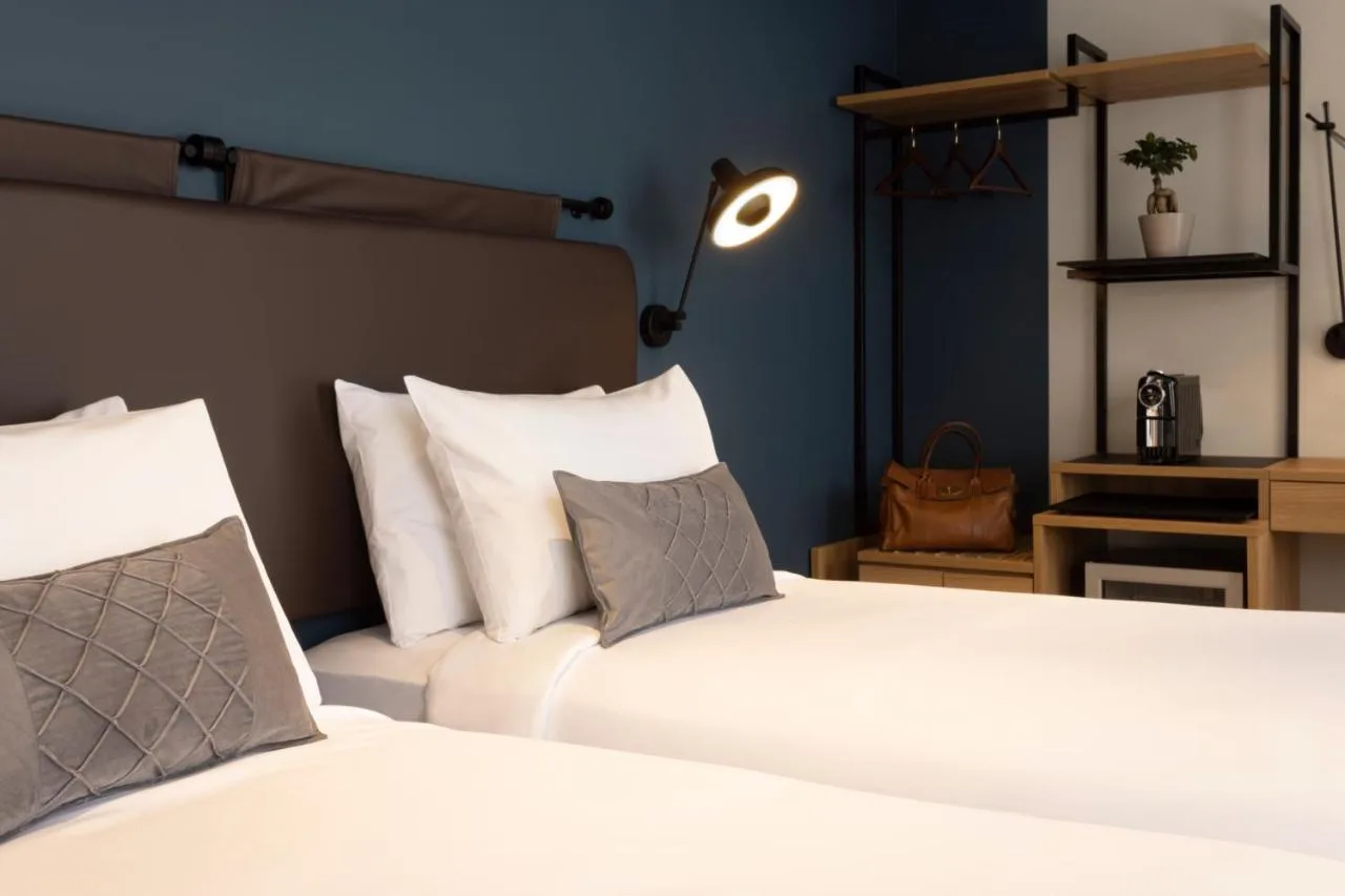 a bedroom with two beds with white pillows and a lamp at The 55 by Le Mirage in London