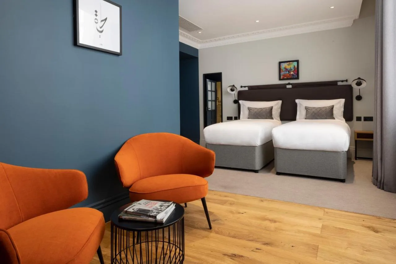 a bedroom with two beds and a chair at The 55 by Le Mirage in London